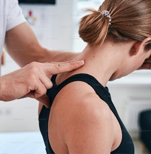Therapist applying shoulder and neck pressure to a woman during a treatment session in a clinic setting.
