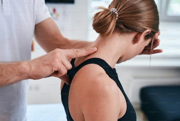 Therapist applying shoulder and neck pressure to a woman during a treatment session in a clinic setting.