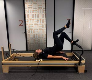 Person on a Pilates reformer performing a leg-raise exercise with hips lifted against the carriage in a studio.