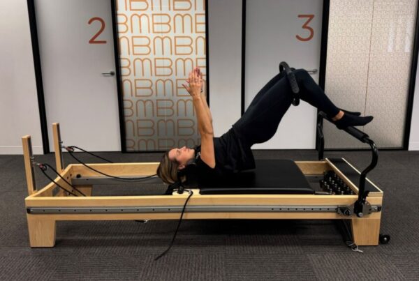 Physiotherapist guiding a client through glute strengthening Pilates exercises on the Reformer at Bend + Mend, Sydney CBD