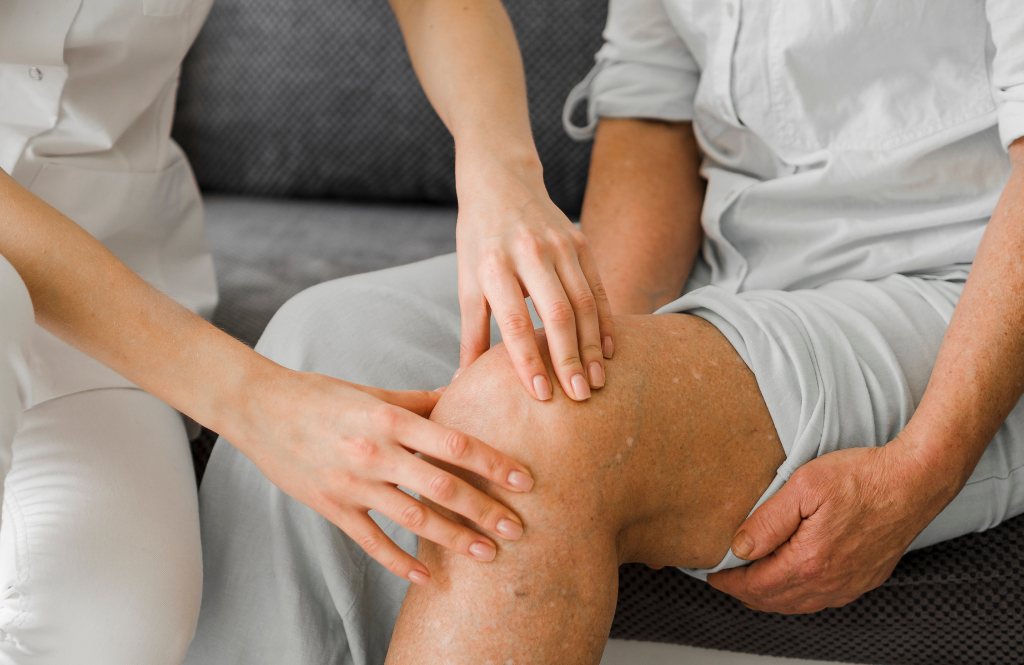 Two healthcare workers gently palpate an elderly patient's knee during a medical examination.
