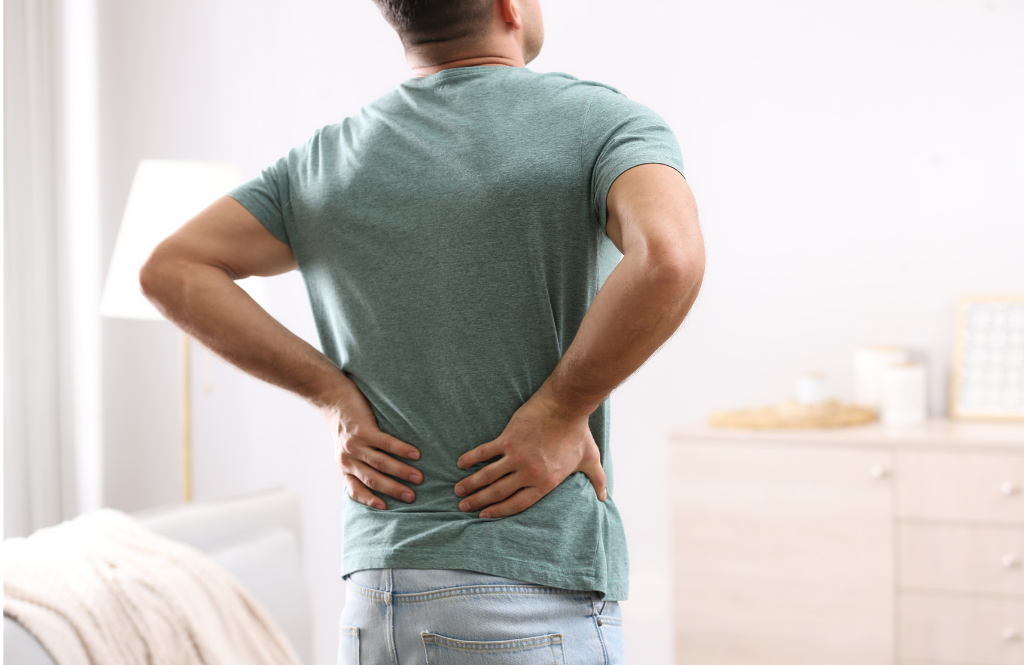 Man standing with hands on his lower back, signaling back pain in a home interior