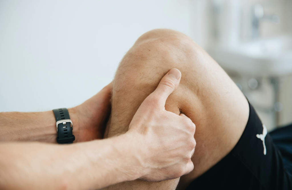 Close-up of a knee being pressed by a hand, wearing a black wristwatch on the wrist.