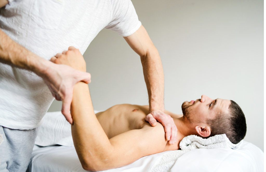 Therapist stretches a male client’s arm during a physical therapy session on a massage table.